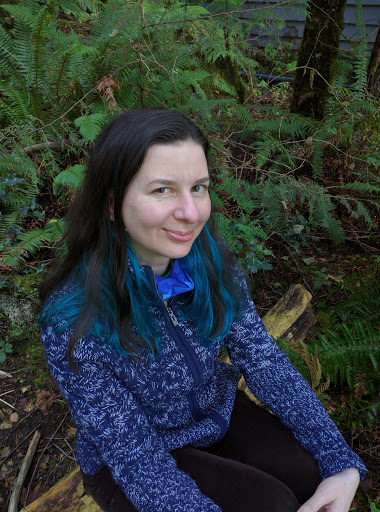 Image of author smiling while seated on log surronded by bracken in a peaceful forest.